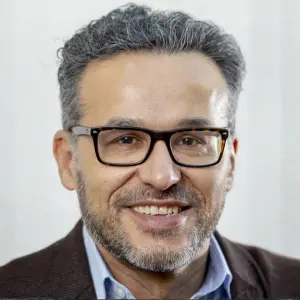 Close up portrait of Marcelo Jenny wearing dark rimmed glasses, a blue shirt and a dark jacket. Photo by Alena Klinger.